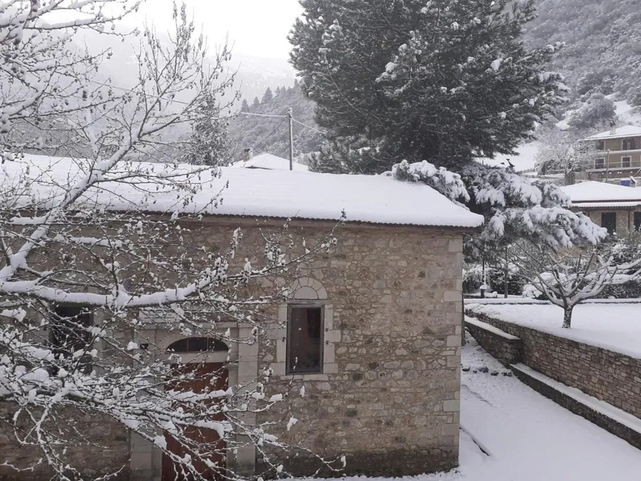 Το πέτρινο σπίτι χιονισμένο, ανάμεσα σε έλατα
